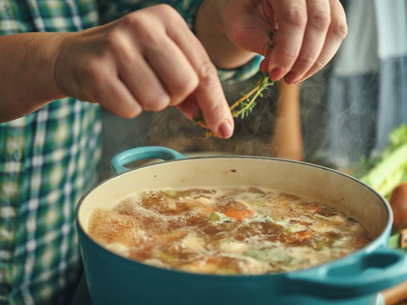 adding herbs to broth cooking in pot on stove