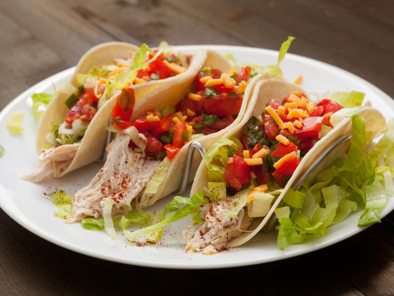 three chicken tacos on a plate topped with tomatoes lettuce and cheese