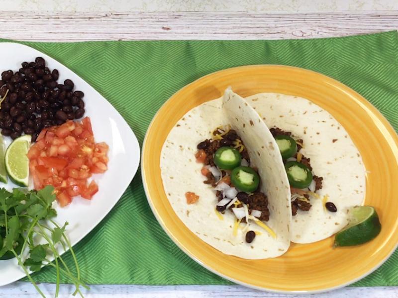 yellow plate with two tacos and assorted toppings on plate to the side