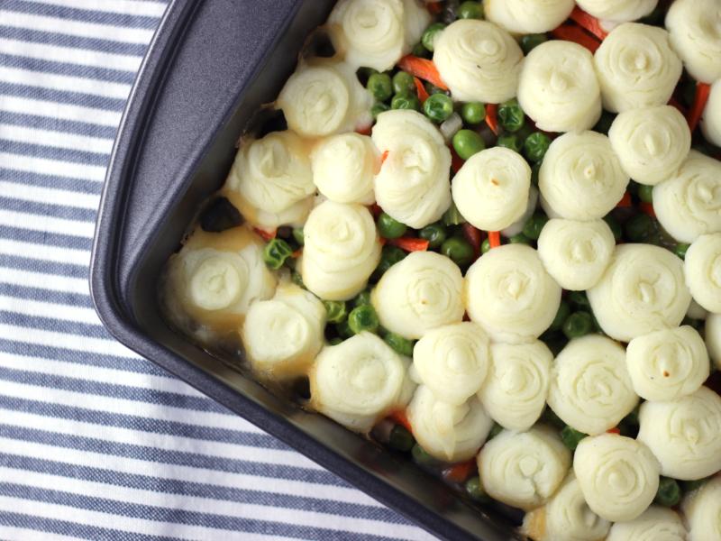 pan of cooked turkey, gravy, and vegetables topped with mashed potatoes